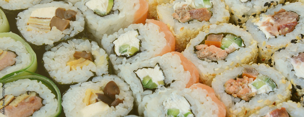 Close-up of a lot of sushi rolls with different fillings lie on a wooden surface. Macro shot of cooked classic Japanese food with a copy space. Close-up of a lot of sushi rolls with different fillings lie on a wooden surface. Macro shot of cooked classic Japanese food with a copy space.