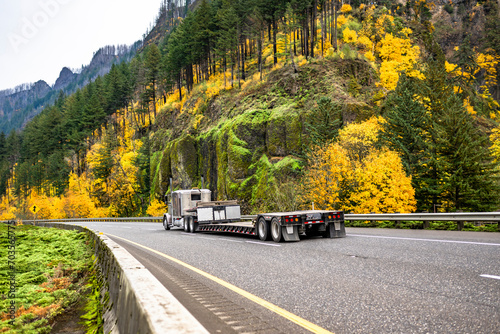 Beige classic big rig semi truck with empty step deck semi trailer driving on the autumn highway road in Columbia River Gorge area photo