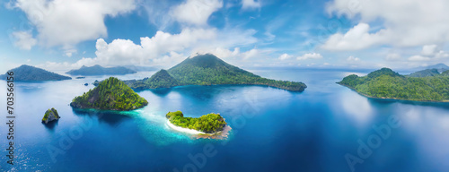 Lush green islands surrounded by the vibrant blue of the Indonesian sea in the Moluccas create a breathtaking panorama. Tropical exotic landscape from above. Aerial view.
