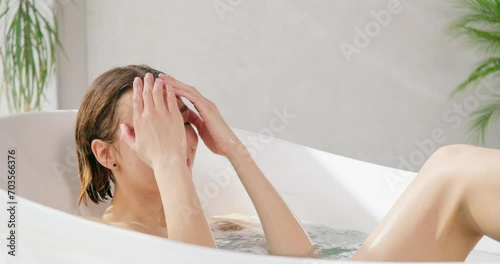 Attractive young woman relaxing, while taking bath at home. Stunning caucasian lady enjoying bathing in modern bathtub at luxury resort, in slow motion. Concept of self care, recreation, spa. 