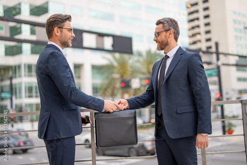 Men in suits handover briefcase outdoor. Business deal. Two business man hold business briefcase. Business transfer deal. Handover of a suitcase in the hands of partners.