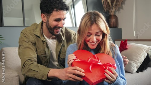 Boyfriend embracing and giving his girlfriend a heart shaped box gift to celebrate Valentines Day. Young couple holding a suprise present on their relationship anniversary. Love and romance date. High photo