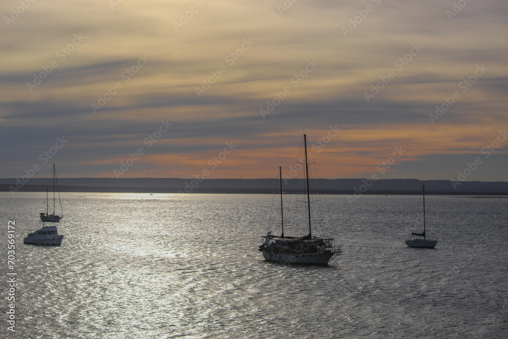 Sailboats in a calm sea under a cloudy sunset.