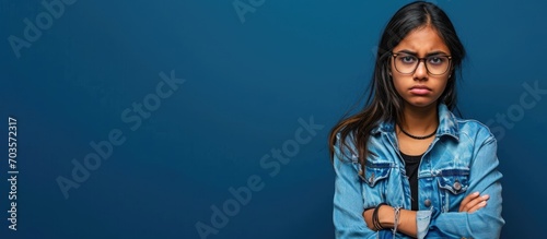 Doubtful young Indian girl in casual clothes, glasses, and disapproving expression, arms crossed. photo