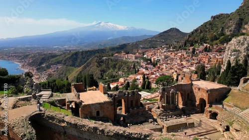 Taormina, Sicily, Italy. Cityscape drone aerial view. Old Greek theatre ruins with active eruption volcano Etna background. Popular travel destination in Europe, UNESCO historical heritage