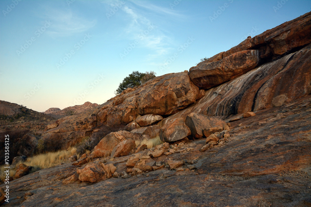 Large boulders are scattered along the rocky mountain slope. Blue sky above