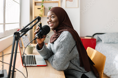 Young african muslim woman recording podcast with laptop and microphone in her room photo