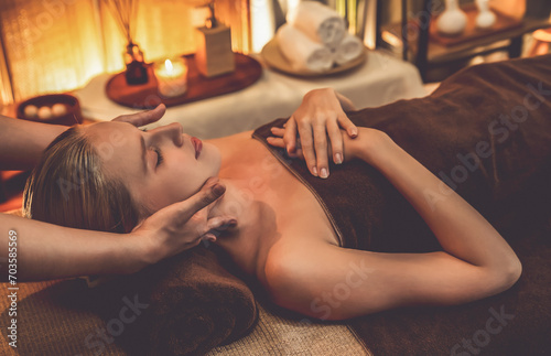 Caucasian woman enjoying relaxing anti-stress head massage and pampering facial beauty skin recreation leisure in warm candle lighting ambient salon spa in luxury resort or hotel. Quiescent