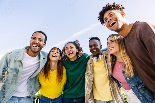 Young group of people having fun together outdoors in a sunny day. Multiracial best friends bonding enjoying time together at city street. United millennial students laughing.