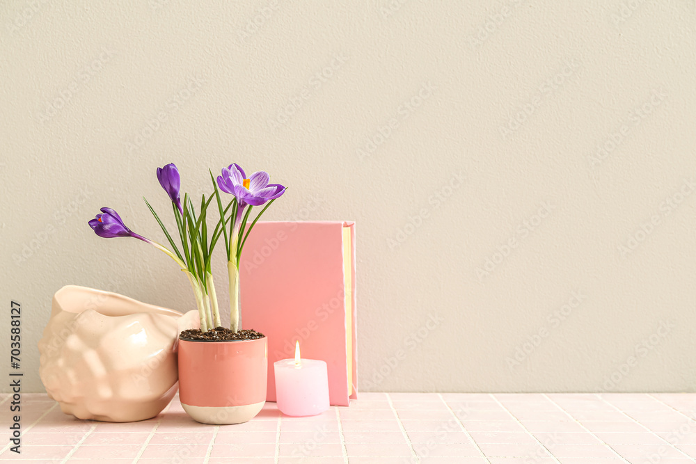 Pot with beautiful crocus flowers, decorative seashell, book and burning candle on table near white wall Pot with beautiful crocus flowers, decorative seashell, book and burning candle on table near white wall