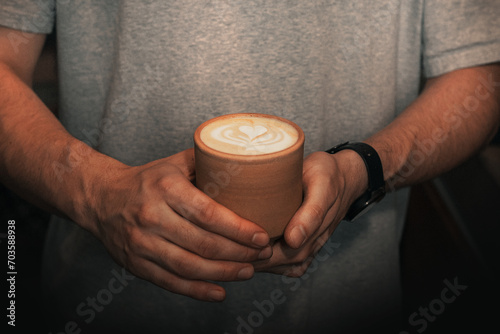 close up of hands holding cup of coffee with milk design