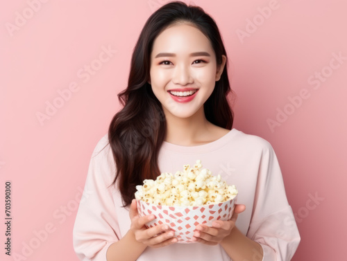 Asian woman holding popcorn in a bowl isolated on pink background