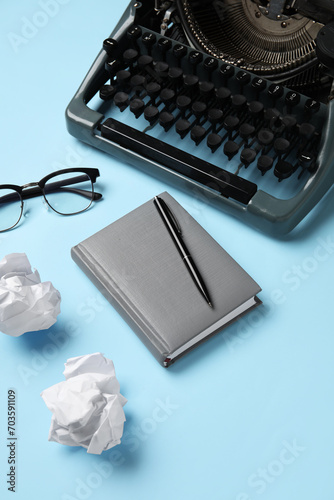 Vintage typewriter with crumpled paper, eyeglasses and notebook on blue background photo