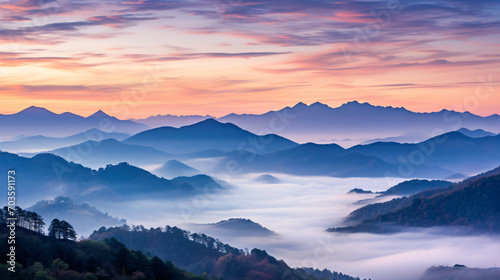 A panoramic view of a mountain range at sunrise with the peaks bathed in a rosy glow and valleys shrouded in mist. © John