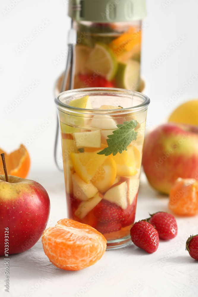 Glass and sports bottle of infused water with different sliced fruits on white table Glass and sports bottle of infused water with different sliced fruits on white table