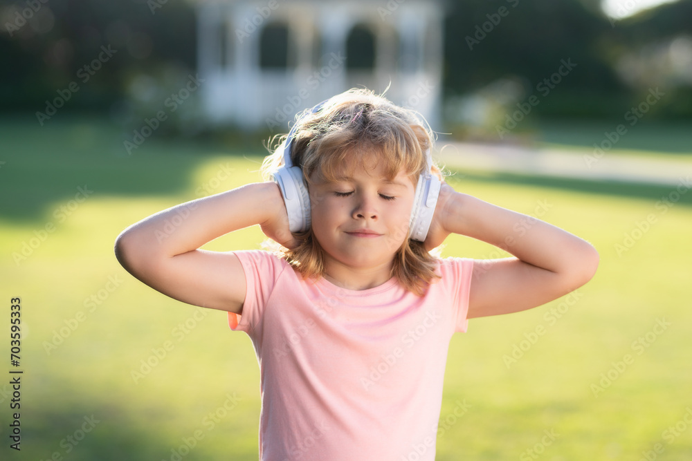 Kid listening to music in headphones. Cute child on summer park enjoy music, dreaming and relaxing. Kid spends free time with favorite music.