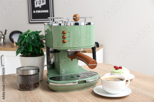 Modern coffee machine with cup of hot espresso and cake on table in kitchen
