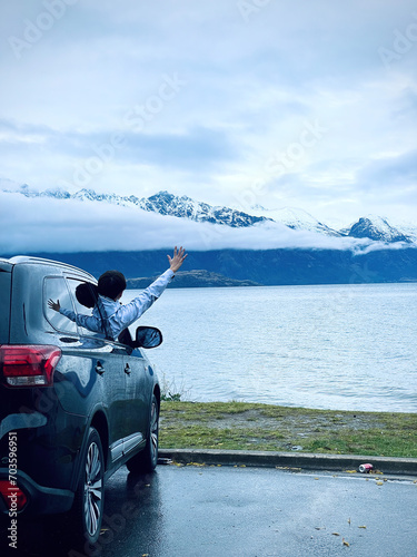 Immerse in the thrill of a solo adventure. A Chinese traveler embraces the scenic road near Queenstown, South Island, with snow-capped mountains framing the journey. Explore the beauty of freedom.