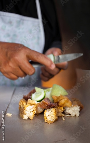 Unrecognizable woman holding knife in her hand and cutting vegetables while cooking vegetable salad near kitchen table, close up © dianeko