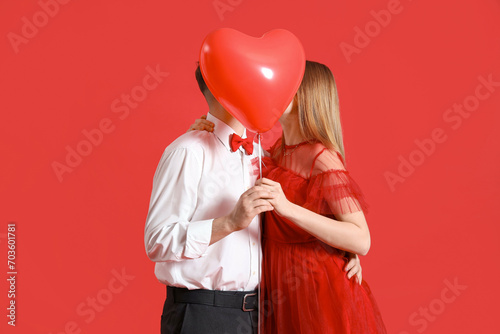 Happy young couple with heart-shaped balloon on red background. Valentine's Day celebration © Pixel-Shot