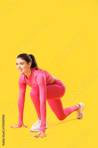 Young woman in sportswear getting ready to run on yellow background