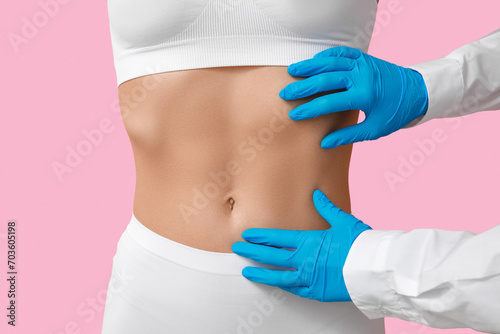 Young woman with flat belly and plastic surgeon on pink background, closeup