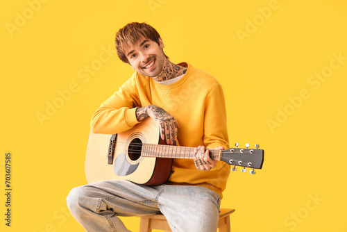 Cool tattooed young man playing guitar on yellow background