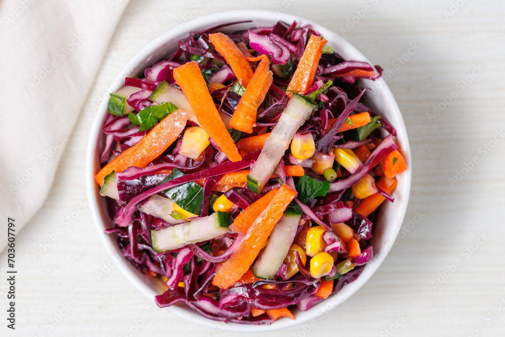 Healthy fresh salad with red cabbage, cucumber, carrot and corn in a bowl on white wooden table. Bright vegetarian food top view close up