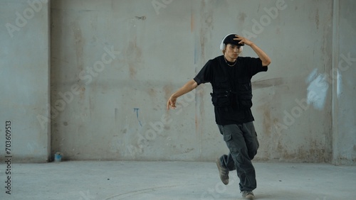 Handsome hipster practicing break dancing while listening music from headphone with cement background. Motion shot of street dancer perform robot dance. Outdoor sport 2024. Modern dance. Endeavor. © Summit Art Creations