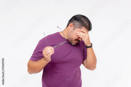 Portrait of a disgraced middle aged man in a purple shirt taking off his glasses, looking depressed. Studio shot on a white background. photo