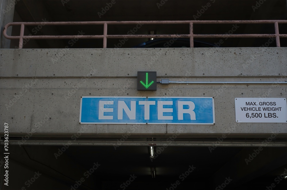 Close up of blue enter sign with green arrow and weight warning sign at a parking garage. Close up of blue enter sign with green arrow and weight warning sign at a parking garage.