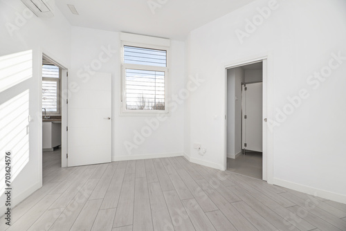 An empty room in a ground floor house with gray parquet floors, white painted walls and access to several rooms