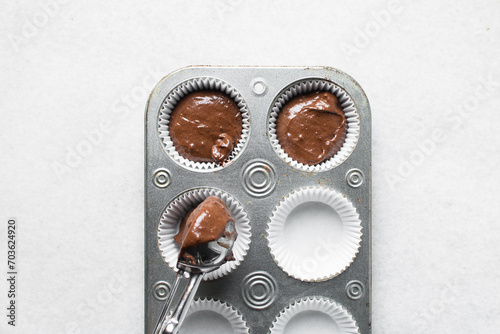 chocolate muffin batter being scooped into a cupcake tin, process of making chocolate muffin