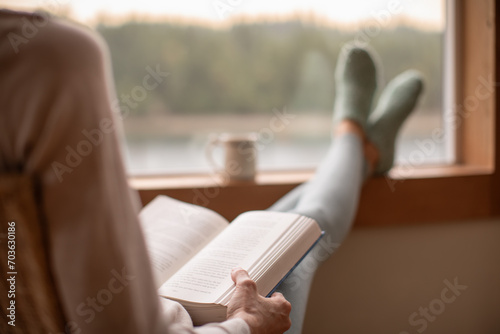 Person relaxing at home reading book feeling relaxed on a cozy winter morning enjoying cup of hot tea or coffee 