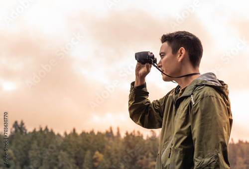 Young man exploring the wilderness travel adventure looking through binoculars