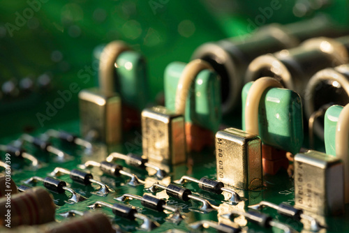 An electronic circuit board made of green fiberglass with many soldered ceramic-painted resistors and capacitors on conductor tracks with color-coded numbers and letters. Computer circuit close-up.