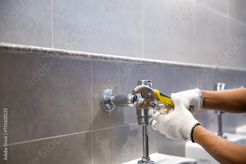 Hand of handyman or plumber is using a wrench to fix or repair leaking water pipes, faucets or valves in toilet bowls and sinks in restroom or bathroom photo
