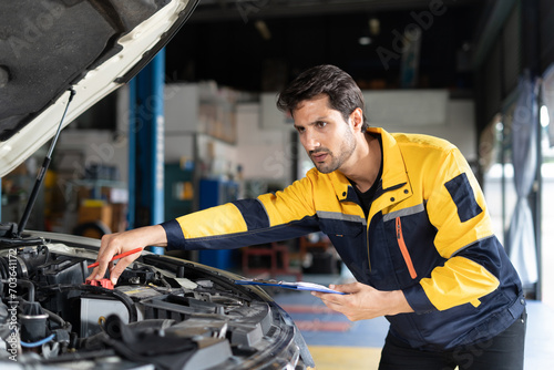 happy latin auto mechanic man checking tires , brakes under car with clipboard in garage cars service . hispanic technician repairing vehicle. lifted car checklist tyres and wheel in auto repair shop