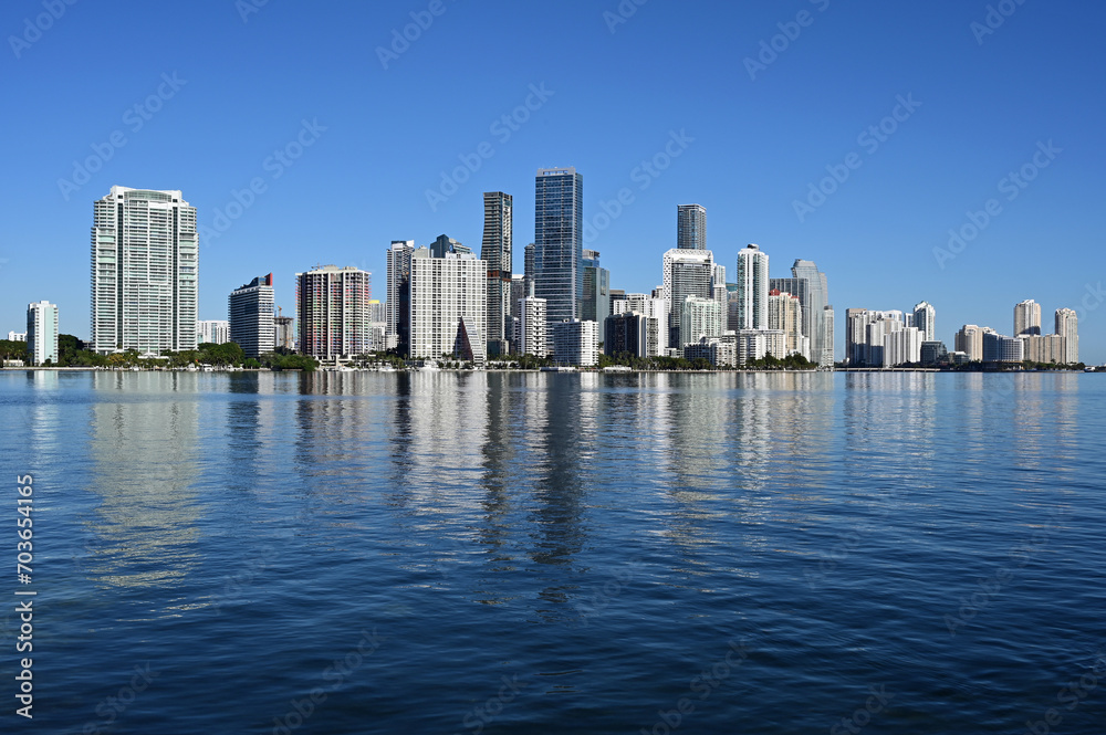 City of Miami, Florida skyline reflected in calm water of Biscayne Bay on calm cloudless December morning. City of Miami, Florida skyline reflected in calm water of Biscayne Bay on calm cloudless December morning.