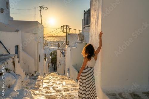 Fototapeta Naklejka Na Ścianę i Meble -  Female tourist exploring Mykonos village streets at sunset. Mykonos island. Greece