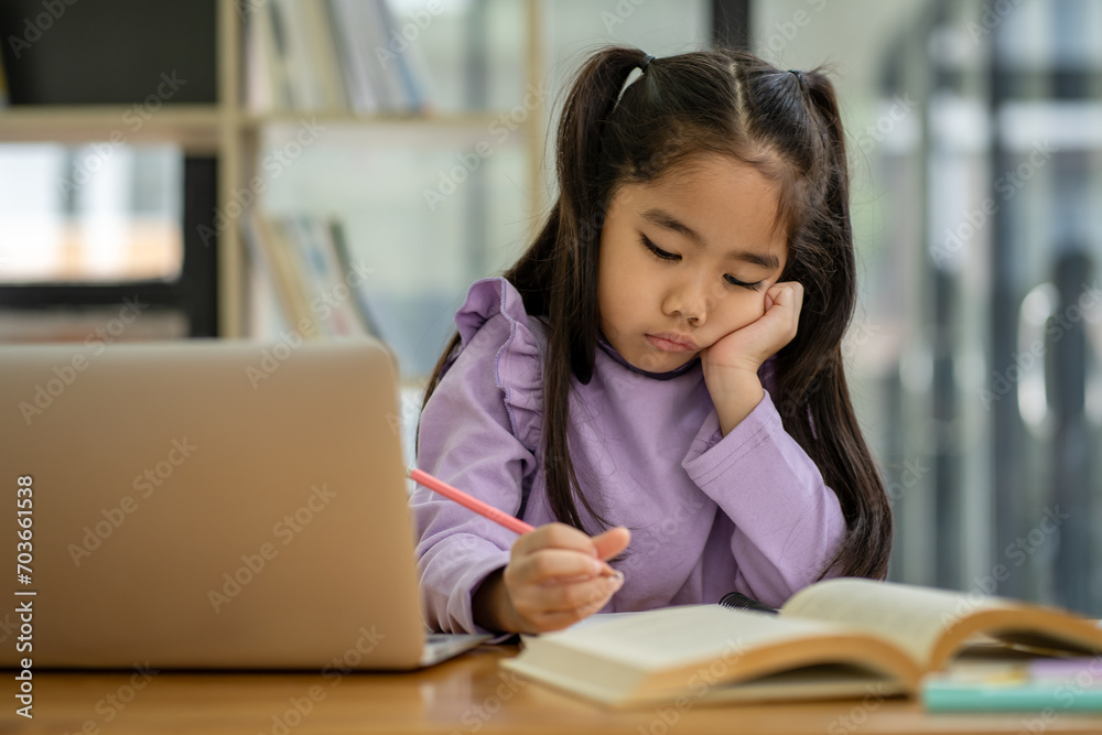 Young Asian girl doing homework online using laptop computer to improve her learning skills. Young Asian girl doing homework online using laptop computer to improve her learning skills.