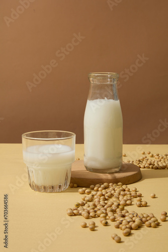 Unlabeled bottle and a glass filled with soy milk displayed with a lot of soybeans on the surface. Template for mockup your design with healthy coarse grains