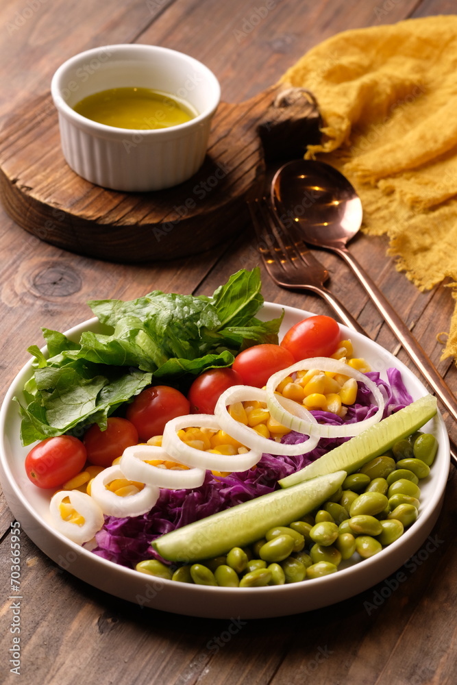 fresh vegetable salad, edamame, sweetcorn, cherry tomatoes, romaine lettuce, sliced cucumber, sliced onions, and purple cabbage. extra virgin olive oil. served on a white ceramic plate. appetizer. fresh vegetable salad, edamame, sweetcorn, cherry tomatoes, romaine lettuce, sliced cucumber, sliced onions, and purple cabbage. extra virgin olive oil. served on a white ceramic plate. appetizer.