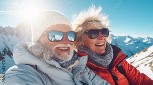 Portrait of old elderly couple at top of snowy mountain for winter sports holidays