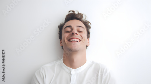 a happy young man with eyes closed smiling lying on white surface, isolated on white background.