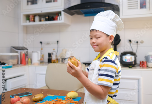 Cute happy smiling Asian 8 years old boy child wearing chef hat and apron having fun preparing, cooking healthy Homemade Japanese Curry Rice at home, Little home helper, EF skill development concept
