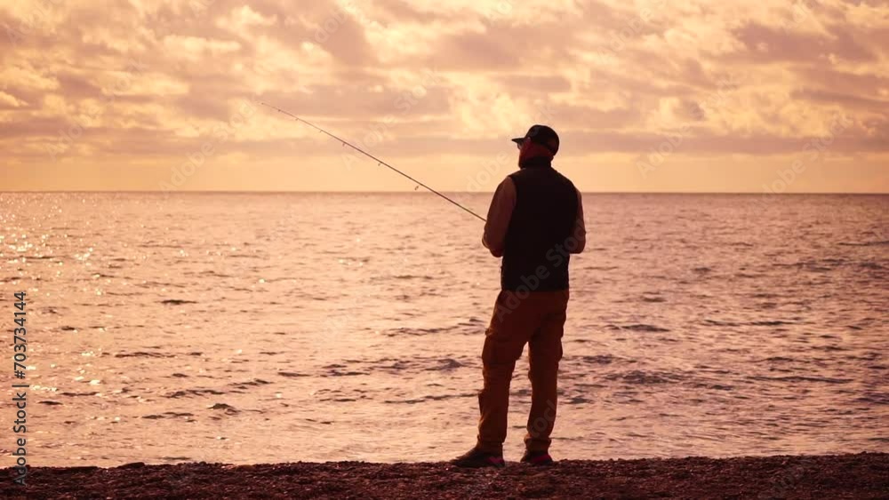 man standing on pier, holding a fishing rod and preparing to cast it into sea ocean at warm sunset. Man hobby fishing on sea tightens a fishing line reel of fish summer. Calm surface sea. Slow motion. man standing on pier, holding a fishing rod and preparing to cast it into sea ocean at warm sunset. Man hobby fishing on sea tightens a fishing line reel of fish summer. Calm surface sea. Slow motion.