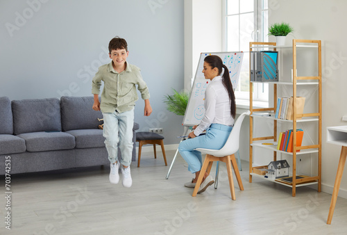 Happy little troublemaker misbehaves at a therapy session. Joyful naughty child boy jumping and having fun during a meeting with a children's therapist or psychologist. ADHD, hyperactivity concept photo