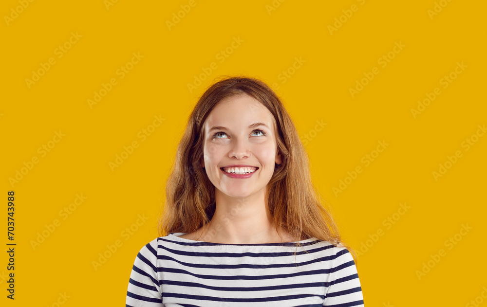 Thoughtful dreaming pensive reflective smiling young woman with wavy long hair in striped sweatshirt looking up on yellow background. Sincere emotions concept. Banner for advertisement, marketing. Thoughtful dreaming pensive reflective smiling young woman with wavy long hair in striped sweatshirt looking up on yellow background. Sincere emotions concept. Banner for advertisement, marketing.