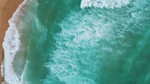 Drone shot turquoise ocean splashing on sand beach. Aerial view foamy sea waves.